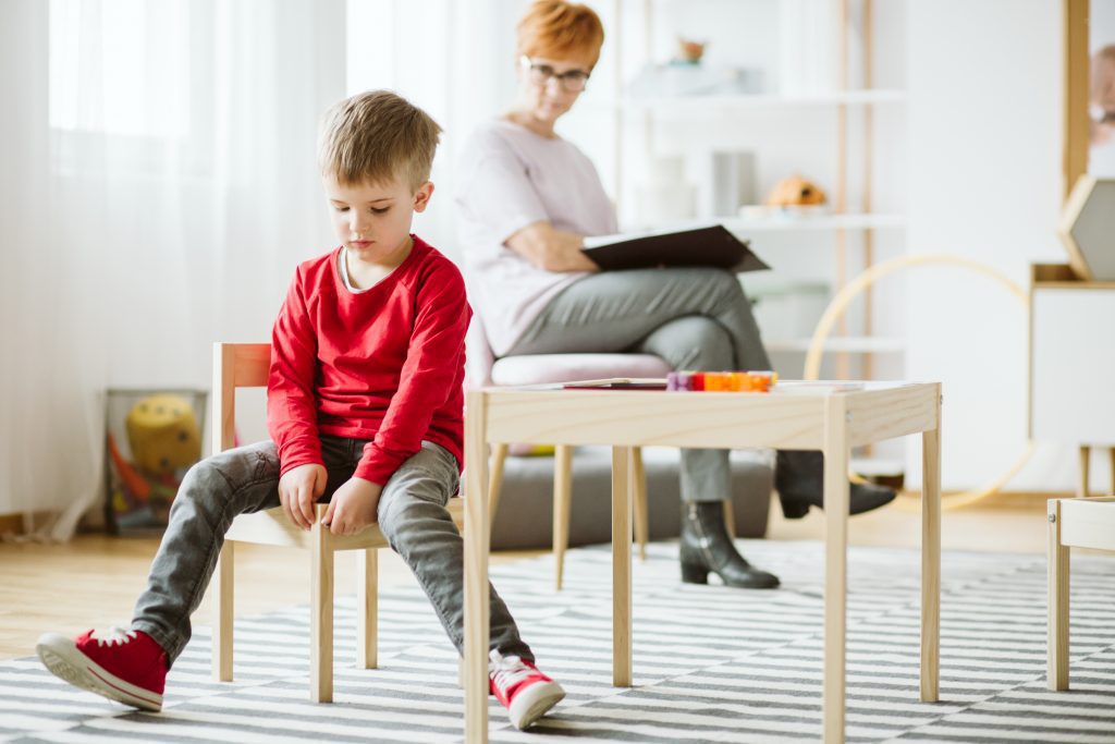 Young boy with autism sitting on a chair in a classroom on a therapy