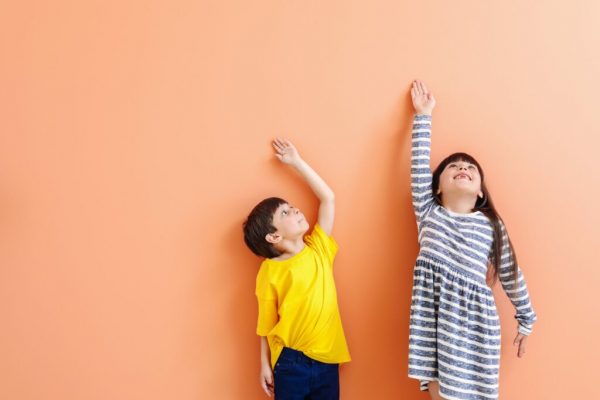 Cute little children measuring height near color wall